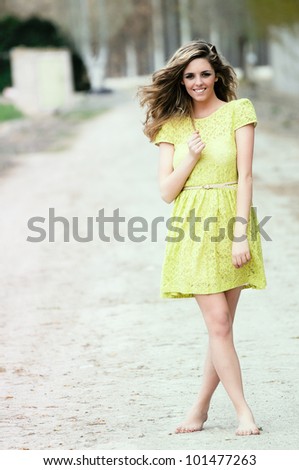 Beautiful blonde girl, dressed with a beige dress, standing in rural road