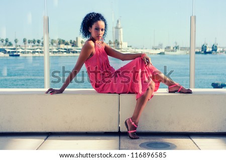 Portrait of a young black woman, afro hairstyle, wearing long pink dress, in the harbor