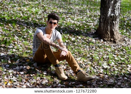 Portrait of a young handsome man, model of fashion, with modern hairstyle in the park