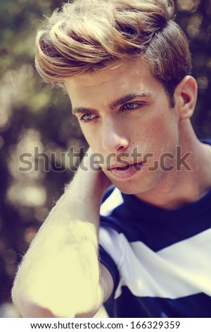Portrait of a young handsome man, model of fashion, with modern hairstyle in urban background. Blonde hair