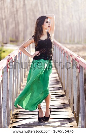 Portrait of beautiful young woman wearing long dress in a rural bridge