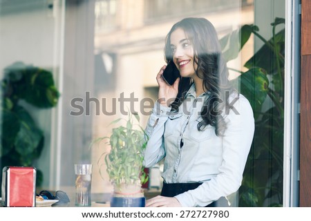 Cafe city lifestyle. Young woman sitting indoor in trendy urban cafe talking with her mobile phone. Cool young modern caucasian female model in her 20s