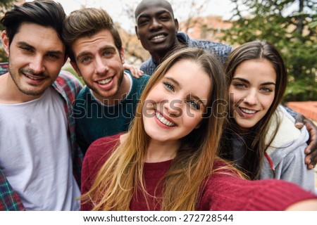 Multiracial group of friends taking selfie in a urban park with a blonde young girl in foreground