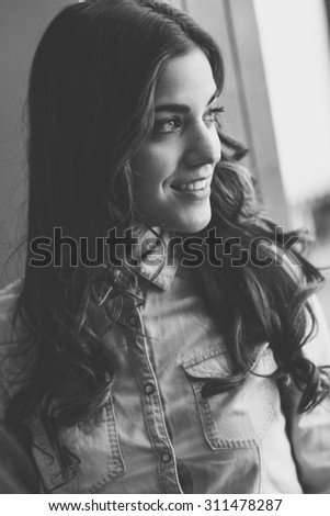 Portrait of beautiful young woman looking through the window wearing denim shirt and smiling