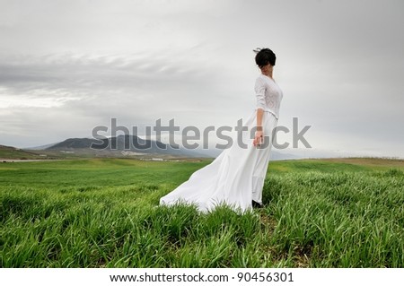 Woman wearing a wedding dress meditating in the meadow against the wind