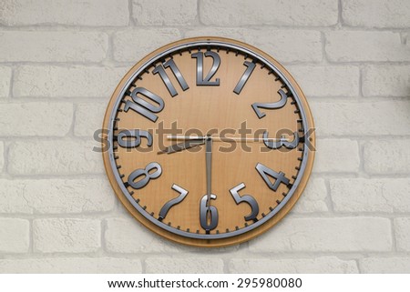 Wooden clock showing eight thirty hanging on white brick wallpaper