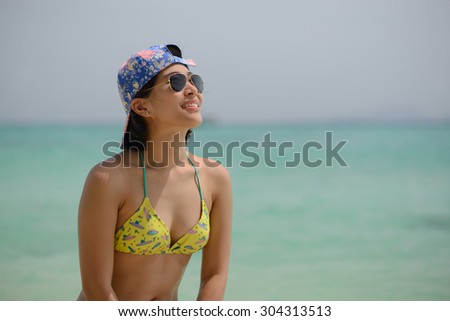 a slim woman wearing top bikini posting at a beach, with flash lens sunglasses, tan skin