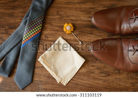 still life men accessories, brown leather shoes, belt, pink bow tie, light brown dotted handkerchief, flower brooch, neck tie, all placing on brown hard wooden floor