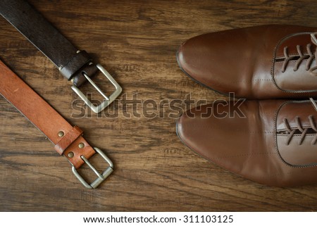 still life men accessories, brown leather shoes, belt, pink bow tie, light brown dotted handkerchief, flower brooch, neck tie, all placing on brown hard wooden floor