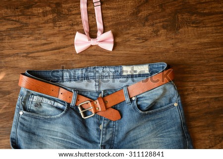 blue jeans with brown leather belt abandoned on hard wooden floor background, pink bow tie