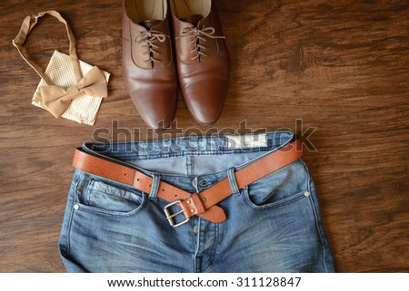 blue jeans with brown leather belt abandoned on hard wooden floor background, brown leather shoes, bow tie and handkerchief