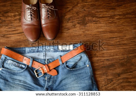blue jeans with brown leather belt abandoned on hard wooden floor background, brown leather shoes