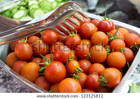 Bowl with a batch of ripe cherry tomatoes with metal tongs