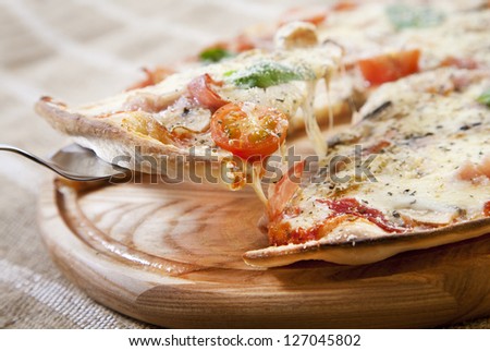 Slice of pizza with ham, vegetables and cheese taken from wooden pizza peel with steel pizza slice server
