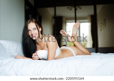 Young beautiful woman sitting in a bed with a white cup of tea or coffee