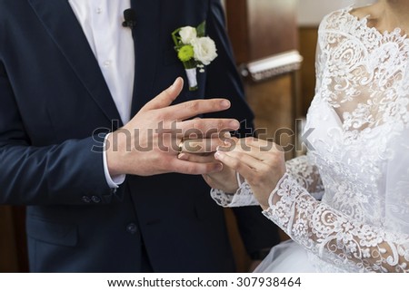 bride\'s hand putting a wedding ring on the groom\'s finger