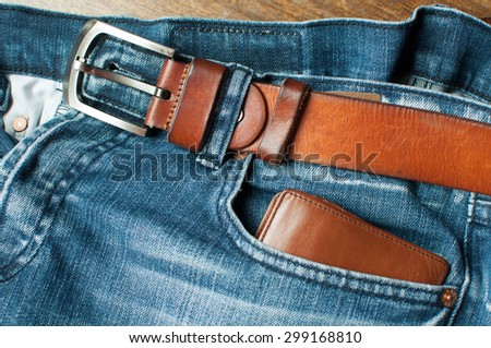 Brown wallet in front blue jeans and brown leather belt