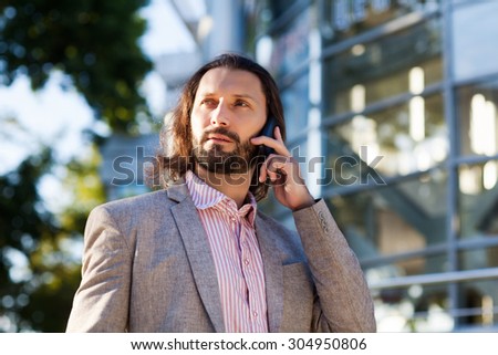 Handsome man wearing suit jacket indoors.  businessman with smart phone talking over office building  business, technology and people concept - smiling