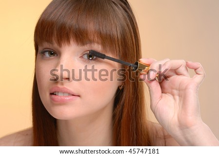 Young beautiful woman making up eyelashes on yellow