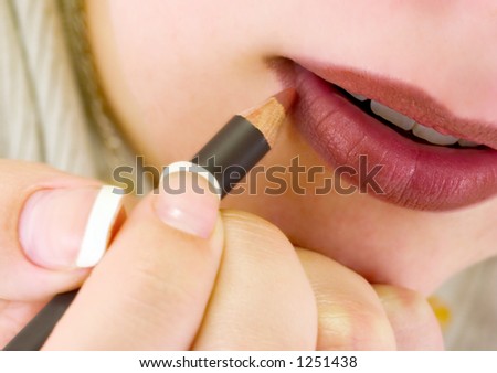 A closeup of a woman putting on lip liner.  Very slight motion blur on the hand and pencil.