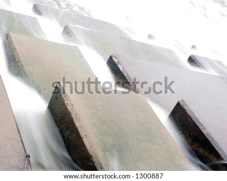 A long exposure of water flowing through the overflows of a small dam.