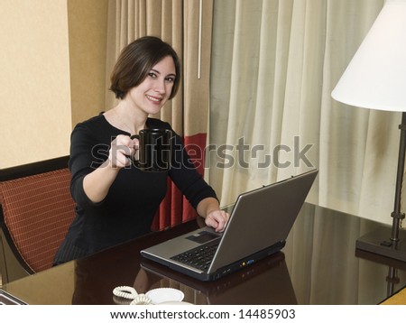 A businesswoman cheerfully reviews good results on her laptop computer in a hotel room during a business trip.