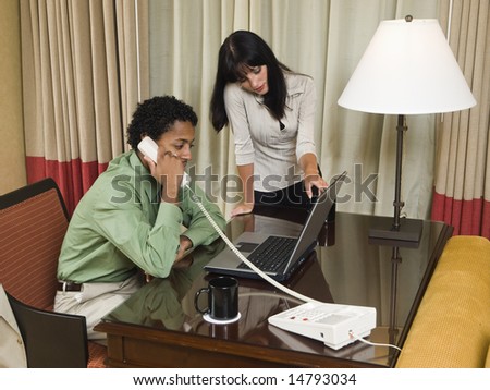 A team of businesspeople review results on a laptop while working late in a hotel room on a business trip.