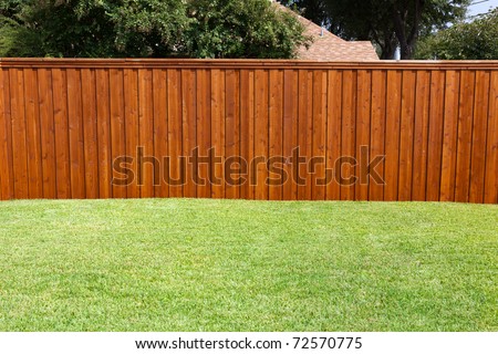 A pleasant sunny backyard with green grass and a nice wood fence.