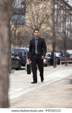 Stock photo of a well dressed Hispanic businessman carrying a briefcase while walking through a downtown business district.