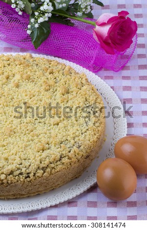Homemade cake presented on a tablecloth with a pink rose and eggs
