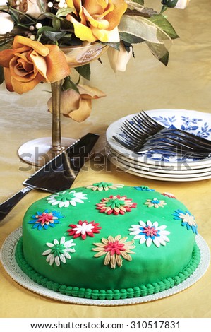 Marshmallow foundant cake decorated with flowers next to saucers silver sweet forks and cake slice