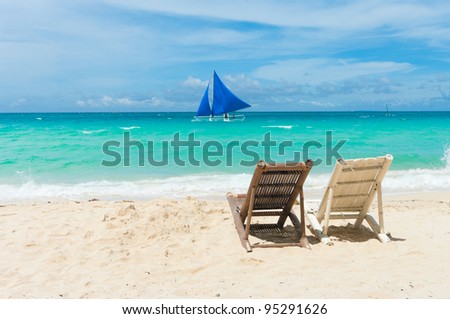 tropical beach with two beach chairs facing the blue sea