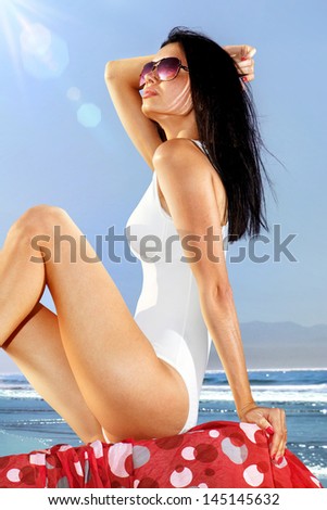 beautiful girl in white swimming suit sits on coast and takes sun bath