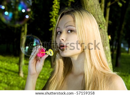 blonde young woman blowing soap bubbles in summer day