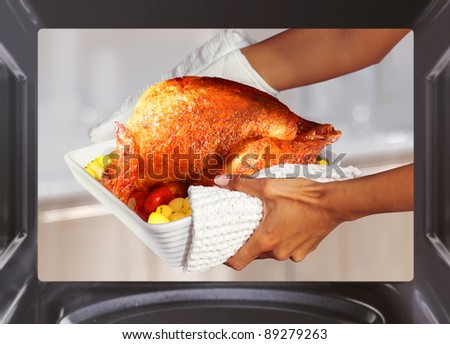 hands of woman is taking out  turkey with potato from oven