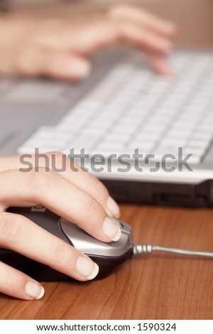 Close-up of a hand on mouse and laptop keyboard in background, blured.