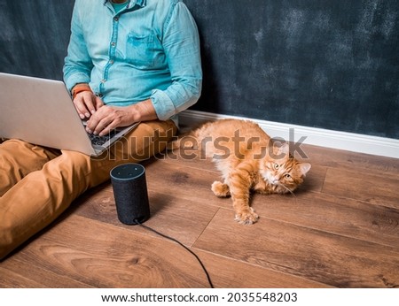 Work from home with funny lazy red cat pet. Man sitting on laminate wooden floor with laptop computer and smart speaker alexa. Ginger pet cat lying. Home office. Remote work Photo stock © 