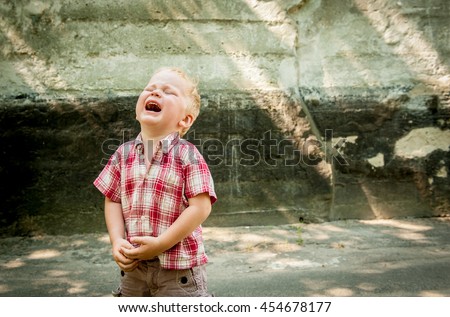 sad and unhappy child boy in the street is crying. Upset problem child with head in hands. concept for bullying, depression stress or frustration. concrete wall as  background