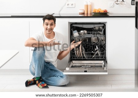 Young smiling man putting dirty plates in dishwasher machine in the kitchen. Household and exhausting cleaning day concept Foto stock © 