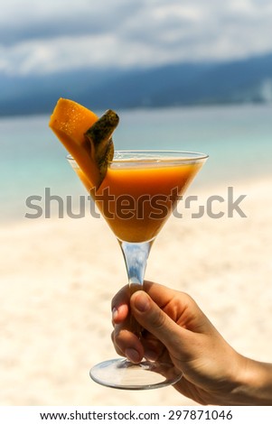 Woman holding a cocktail glass on the beach in Lombok, Indonesia.  Vertical photo with blue sea and sand in the background