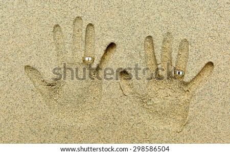 Two Hand shapes in the sand. Each hand has a  golden wedding ring on the fourth finger.