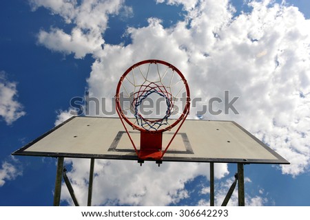 Basketball hoop pictured from the ground with blue skies and white clouds in the background.