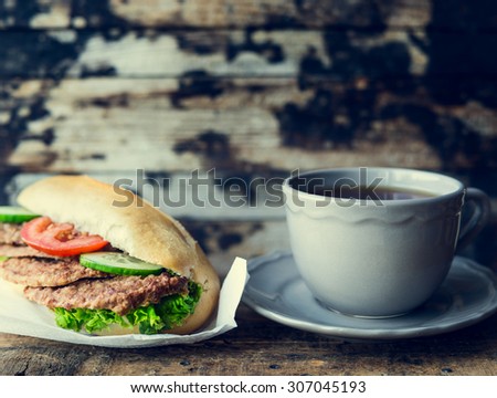 cup of tea and a sandwich with meat on a dark wooden background , toned