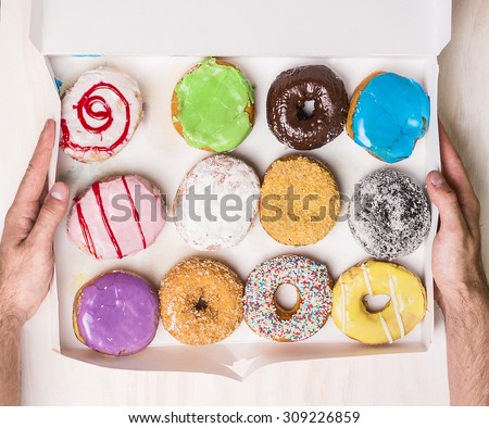 set of donuts in white paper box  in male hands on wooden background, top view, close up