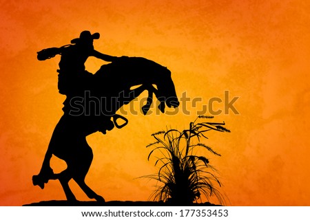 Silhouette of cowboy reigning bucking bronco spooked by something in the nearby sagebrush. Sunset orange/yellow textured background.