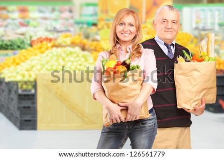 Man and woman in a supermarket holding paper bags with groceries