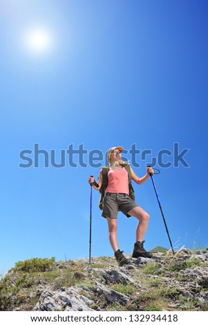 A young female with backpack and hiking poles posing at sunny day in mountain