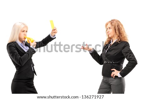 Woman in suit showing a yellow card and blowing a whistle to a female colleague, isolated on white background