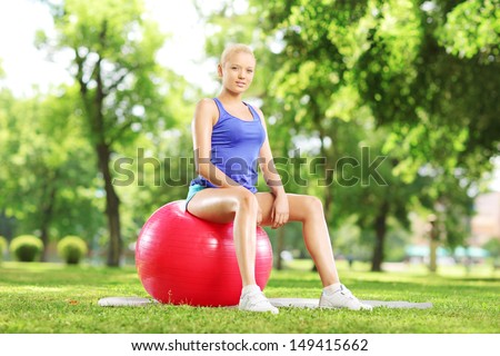 Young female athlete sitting on a pilates ball and looking at camera, in park