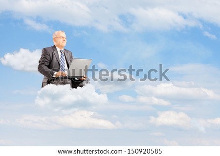 Mature businessman in suit flying on clouds with laptop against cloudy sky